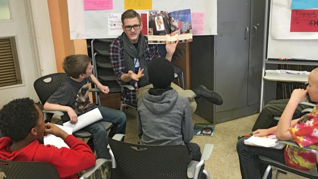 a man sitting in front of a group of kids reading a book