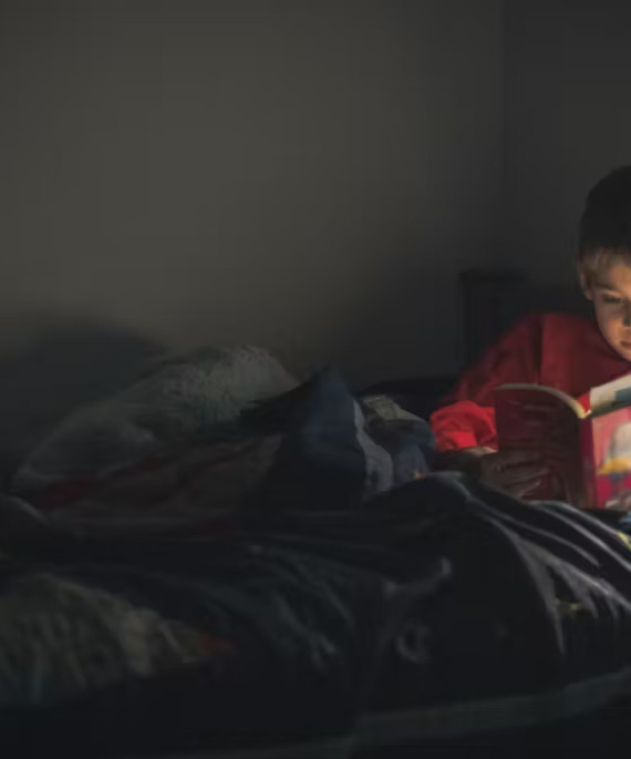 child reading a book in bed with bed side light on