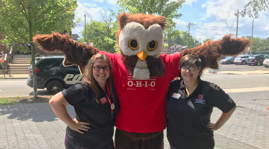 two women stand on either side of a person dressed as an owl for move-in day at Ohio State