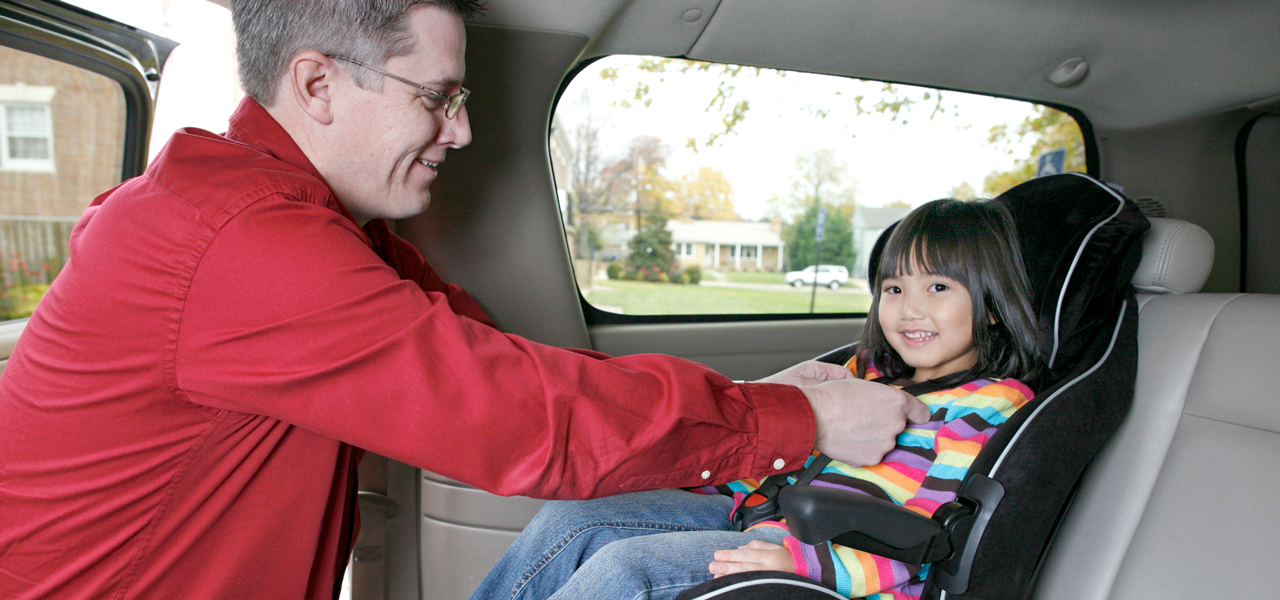 man buckles girl into car seat