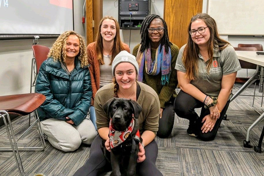 Group of Ohio State women with a black lab puppy