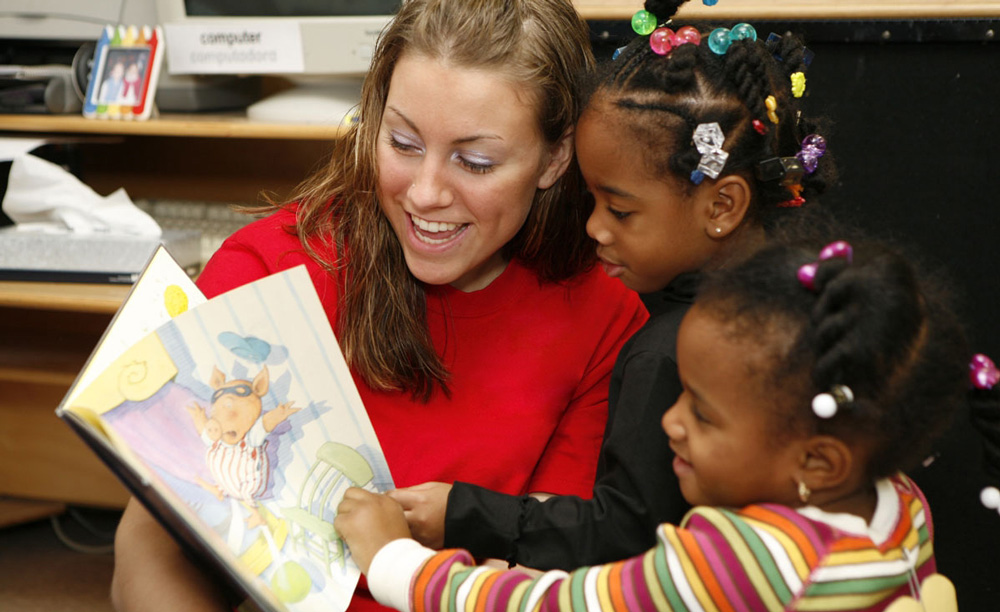 College student reads book to two preschool girls