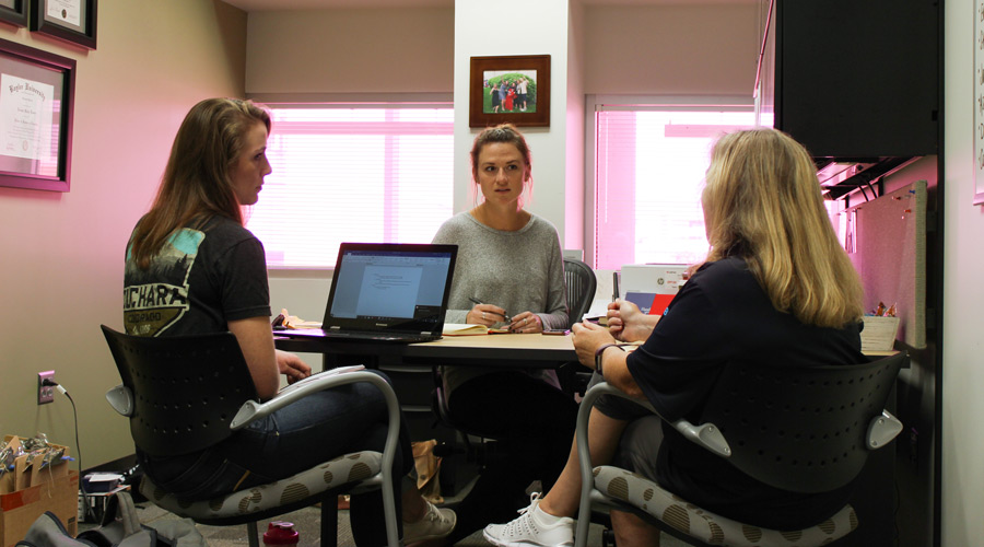 three women sit around a desk discussing work