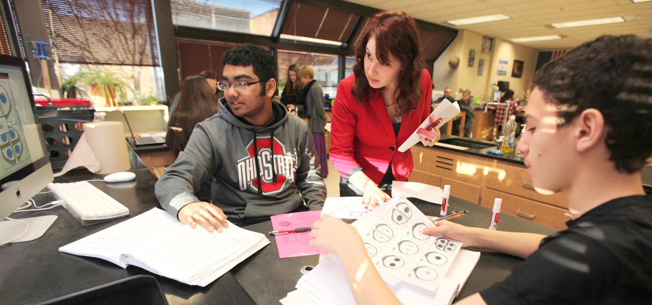 An Ohio State Master of Education student in her field experience helps two high school students with an in-class assignment.