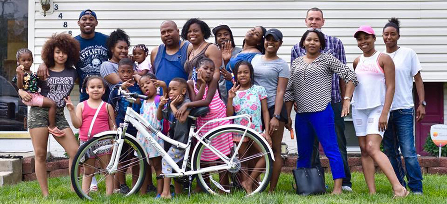 Twenty members of Shelly Martin's family pose with a bicycle outside a house.
