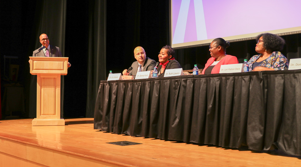 A moderator at a podium asks questions to a four-person panel