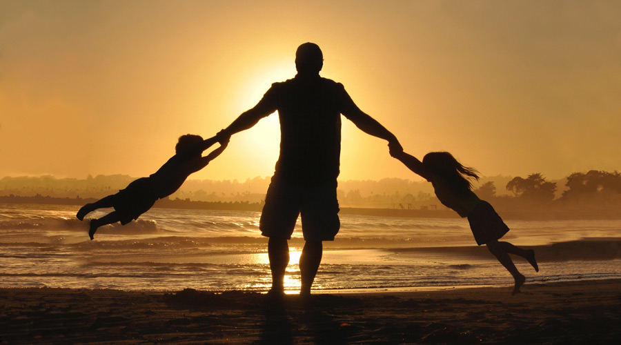 Dad swings son and daughter on his arms at a sunset on the beach