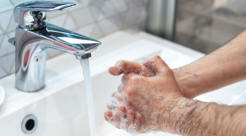 man washing hands in sink with running water