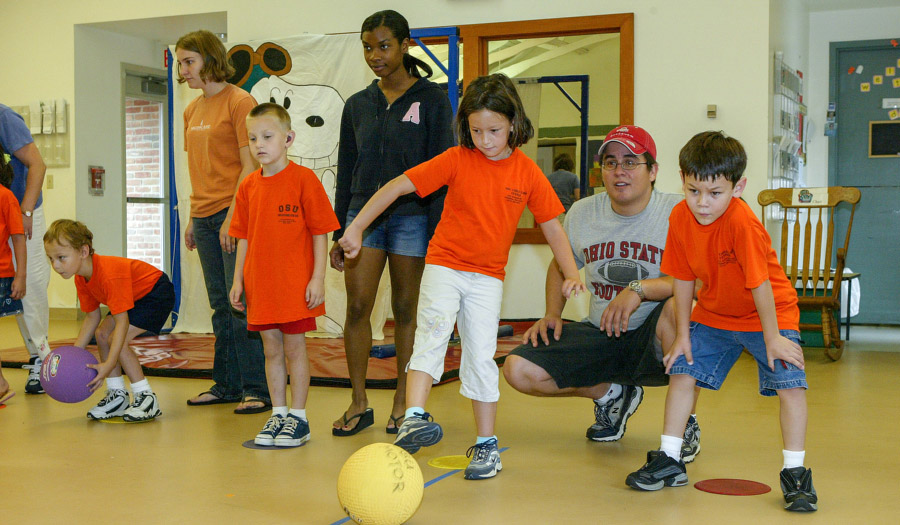 kids practice kicking balls with adult guidance