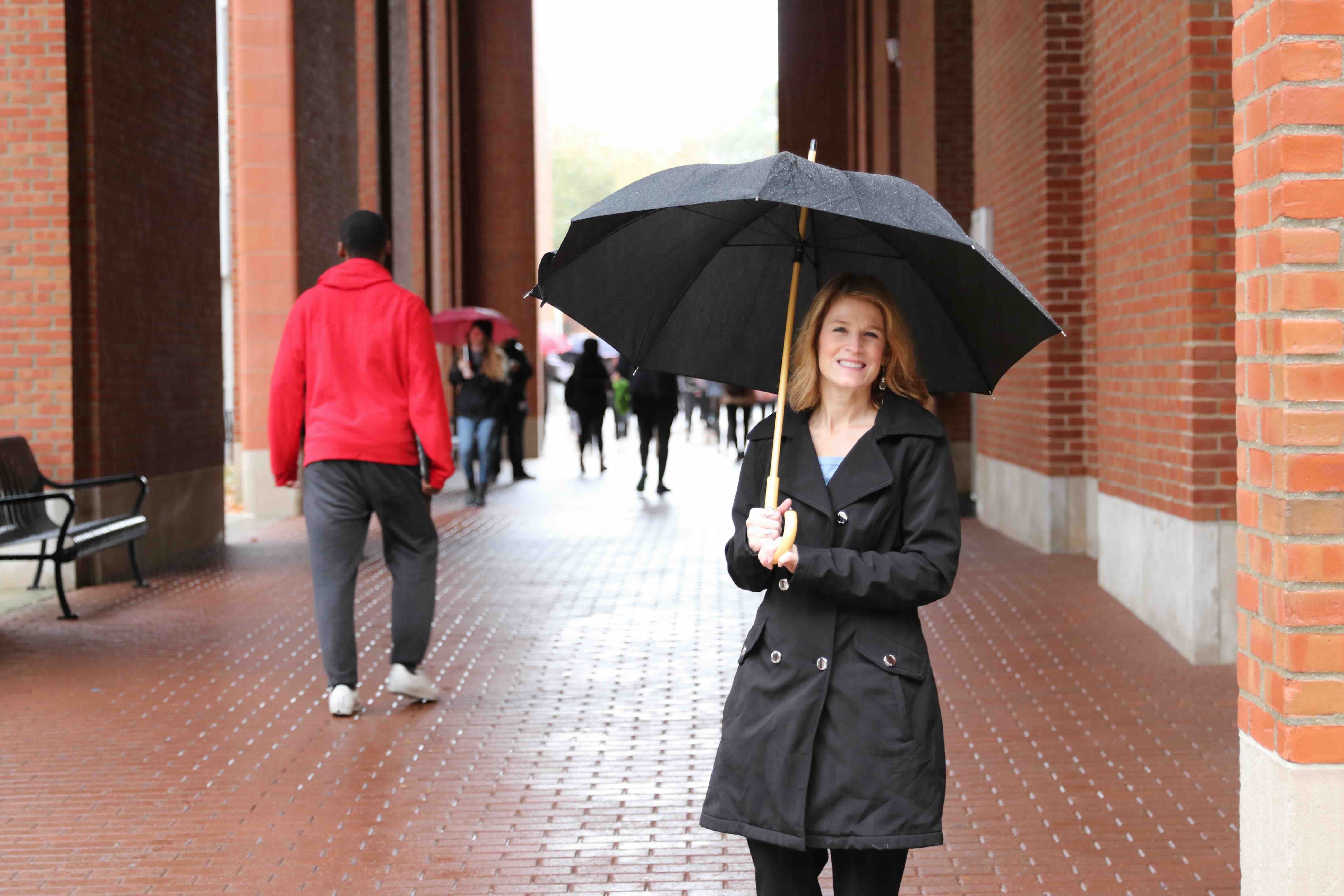 Penny Pasque walking through Ohio State campus in the rain holding an umbrella