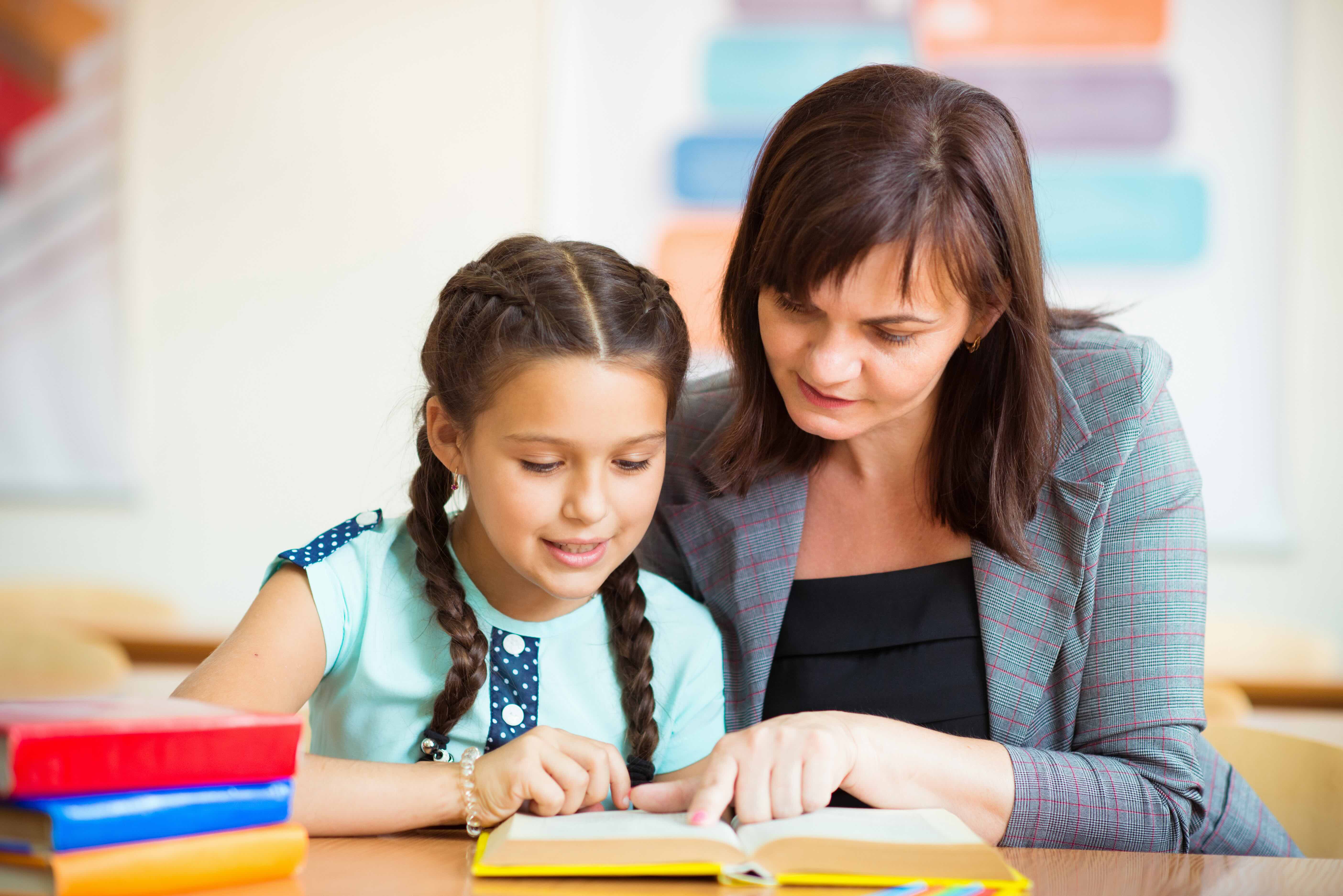 teacher tutoring a child in reading at a school desk