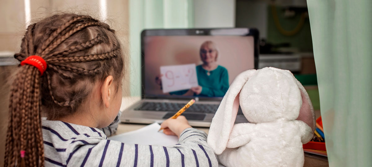 Girl studies math from a teacher online alongside her stuffed bunny