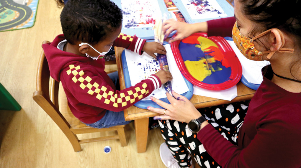 pre-school teacher helping child fingerpaint