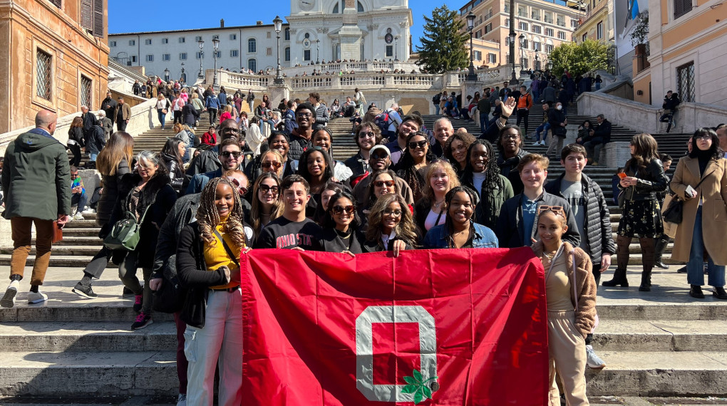 Group of Ohio State students on steps in Spain holding red Ohio State flag.