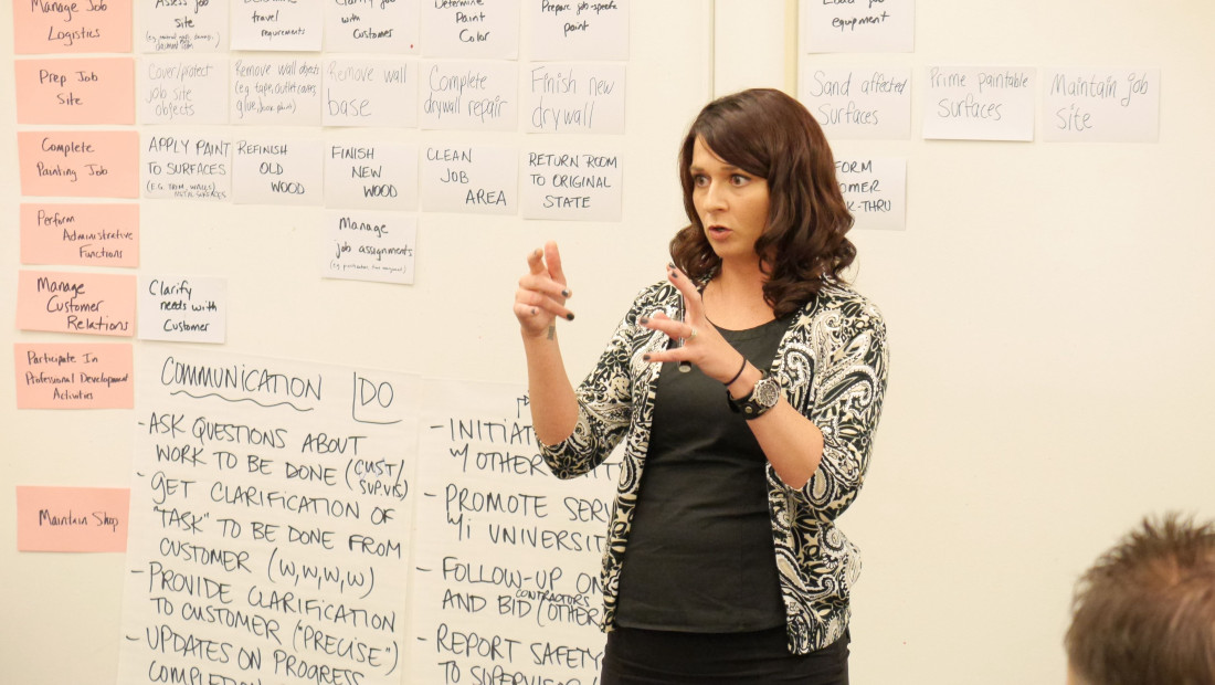 Woman standing in front of a white board speaking to a classroom