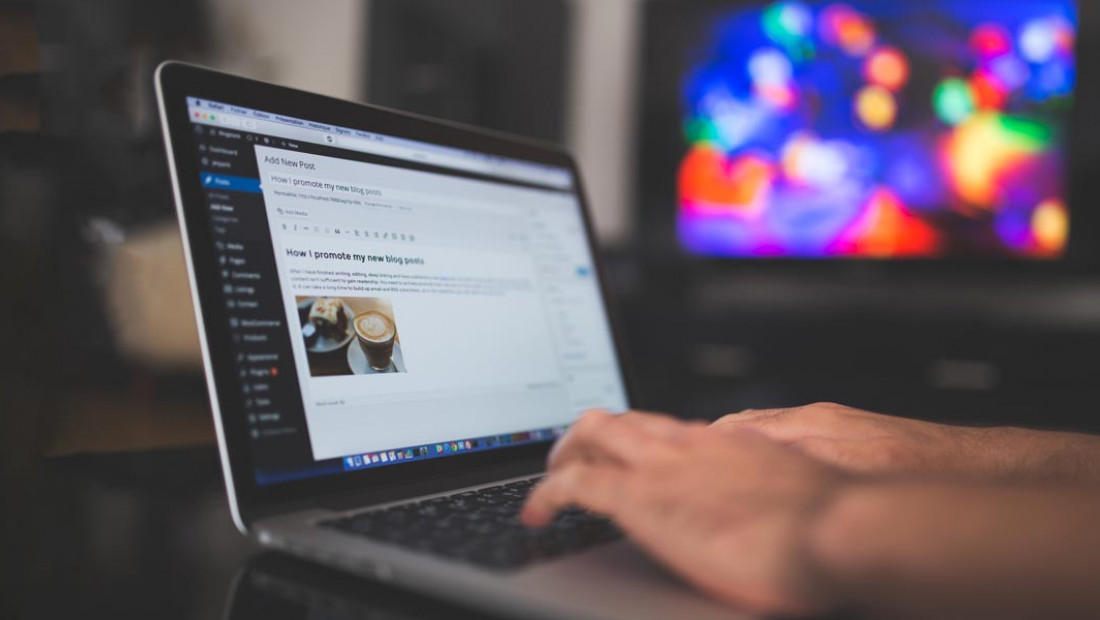 a person typing on a laptop with a television in the background