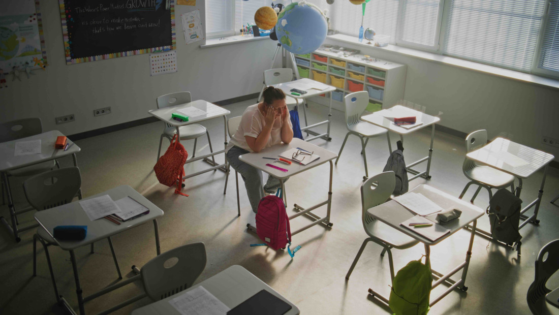 Teacher in an empty classroom with her head in her hands looking disappointed