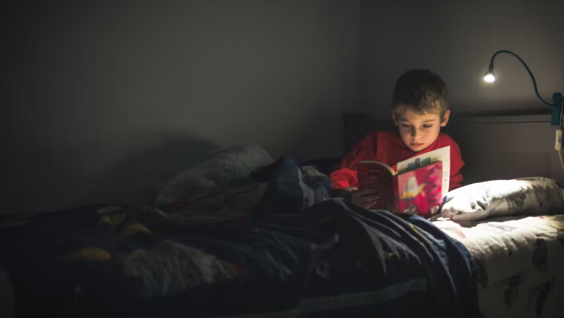 child reading a book in bed with bed side light on