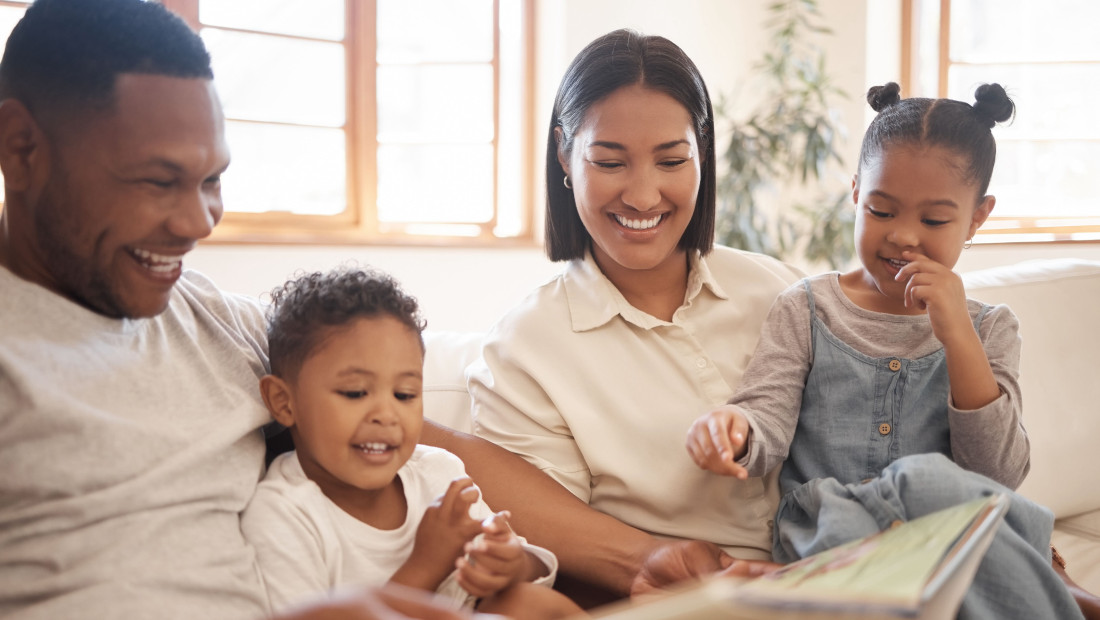 Mother and Father reading a picture book to their two young children on their living room couch