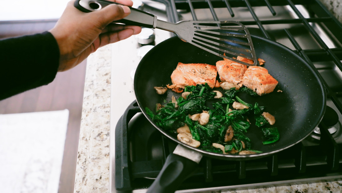Salmon and greens being cooked in a pan on a stovetop
