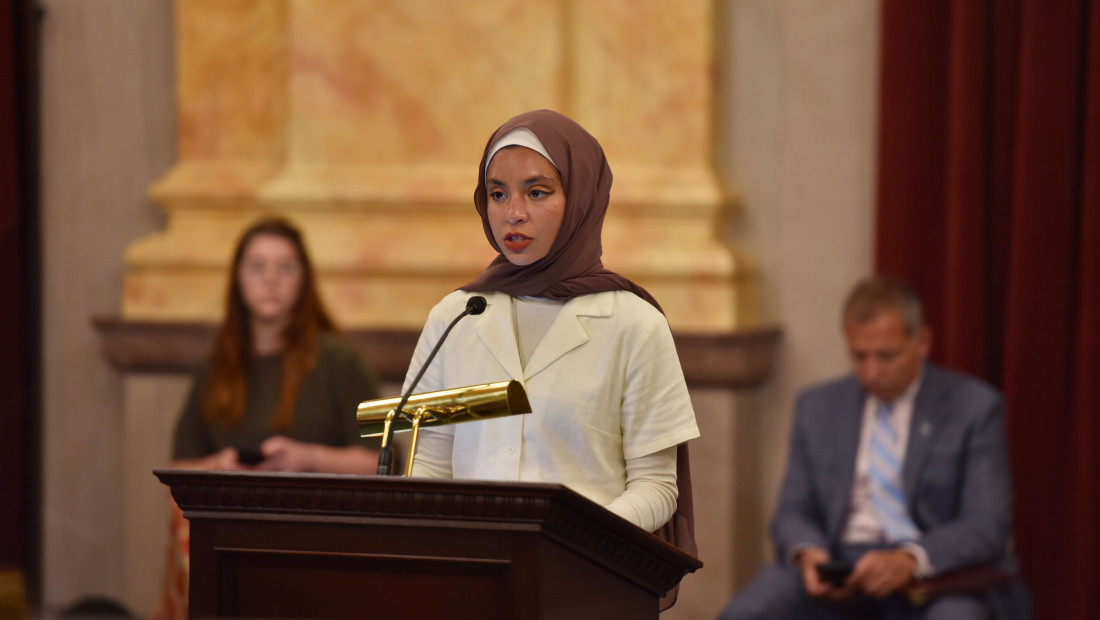 Noor Alexandria Abukaram at speaking at a podium in the Statehouse