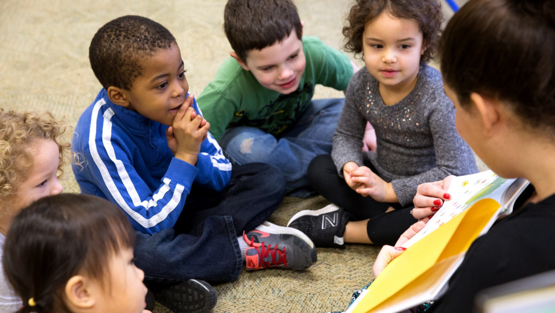 children sitting around teacher who is reading a picture book aloud