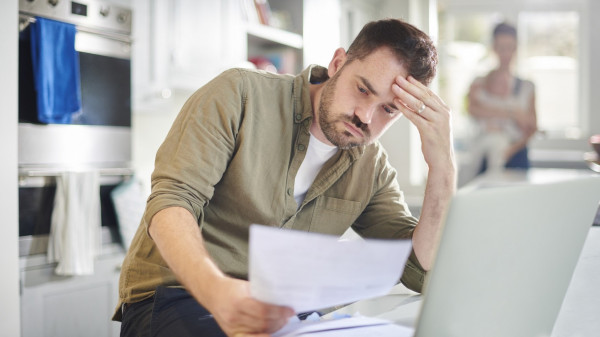 man reviewing documents are kitchen counter with open laptop