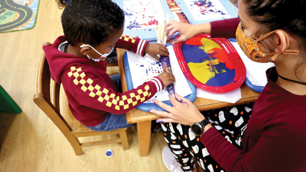 pre-school teacher helping child fingerpaint