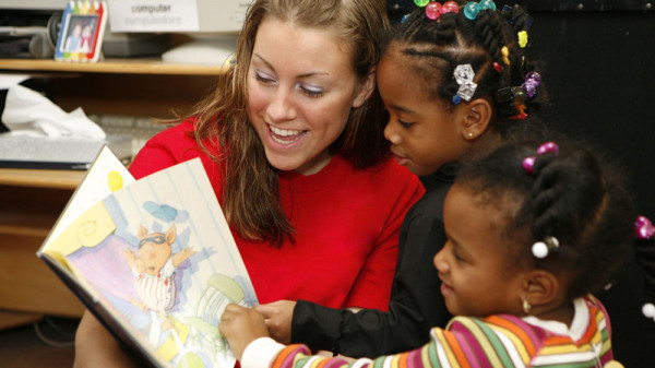 Teacher reading a book to two young students