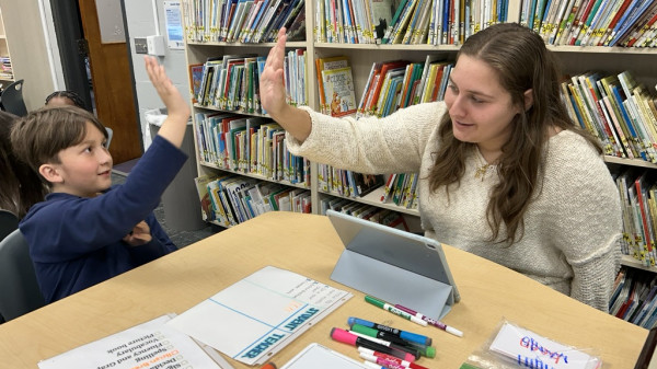 Teacher high-fiving a young student while working on schoolwork in a library