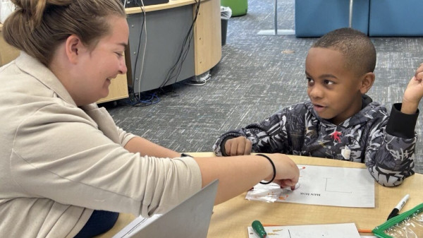 teacher working with a young student at a desk filling in a worksheet