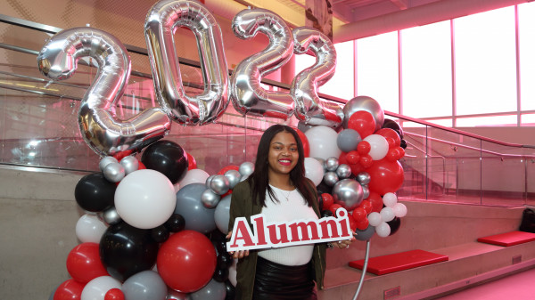 student holding alumni sign under balloons