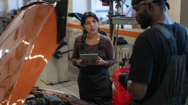 Man and woman mechanics looking at a car with the hood open