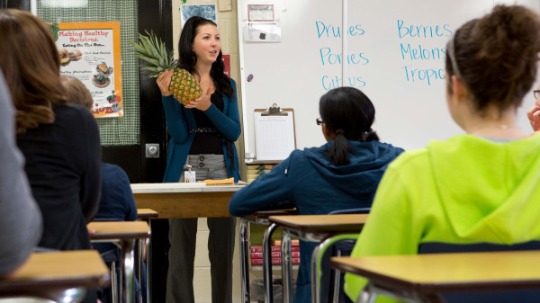 Teacher in front of home economics class demonstrating how to cut fruit