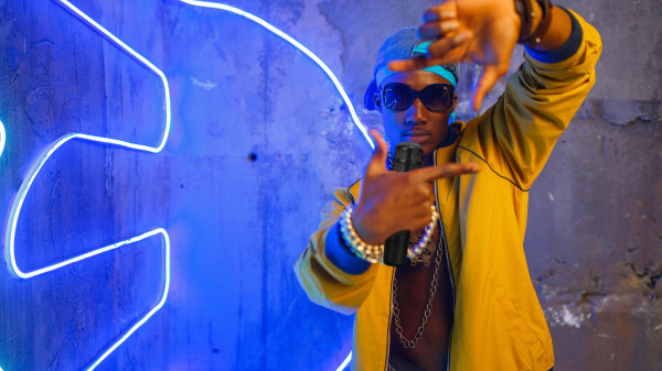 Rapper standing next to neon lights with a microphone