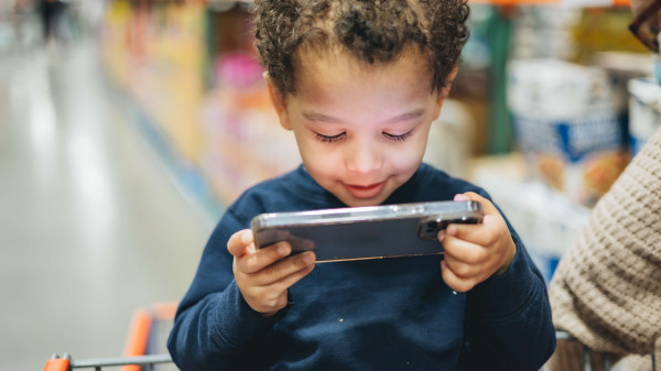 Young child in shopping cart looking at a phone