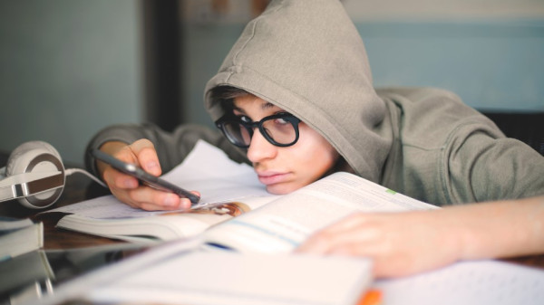 Student in a hoodie looking at their smartphone while doing school work