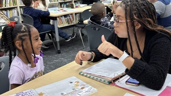 teacher working with young student on a reading assignment in a classroom