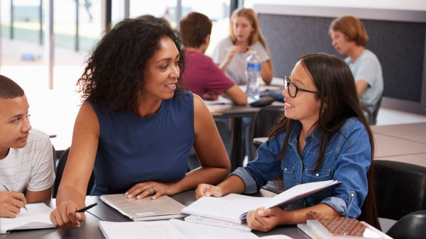 A teacher studying school books in a classroom with students.