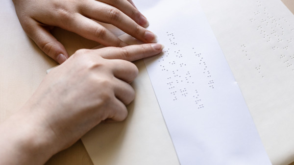 woman reads note in braille on sheet of paper