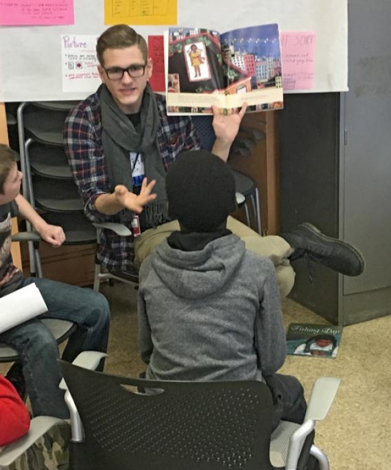 a man sitting in front of a group of kids reading a book