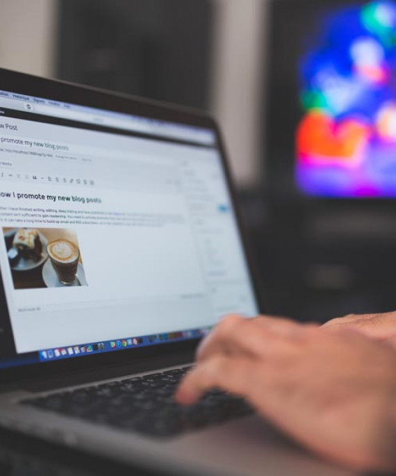 a person typing on a laptop with a television in the background