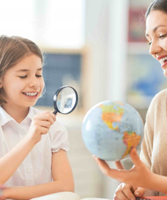 Girl with teacher in the classroom studying globe