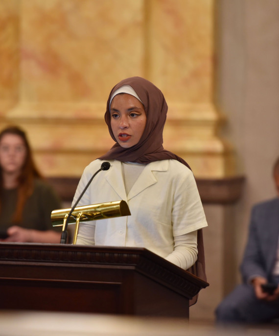 Noor Alexandria Abukaram at speaking at a podium in the Statehouse