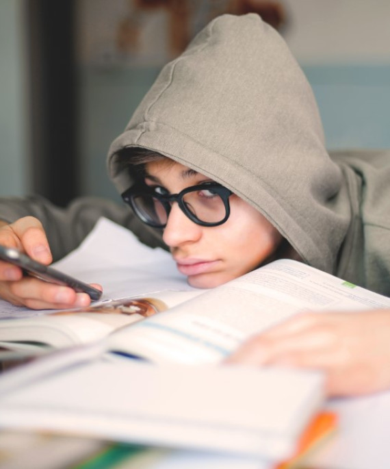 Student in a hoodie looking at their smartphone while doing school work