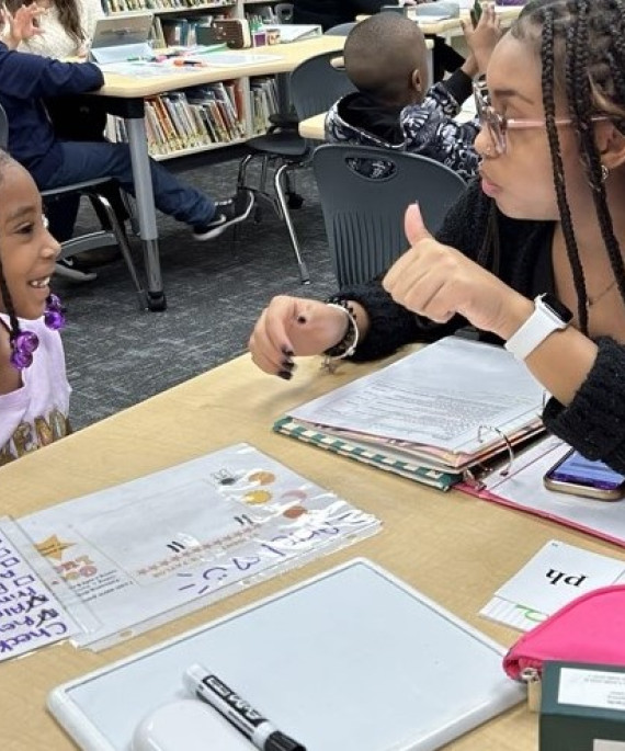 teacher working with young student on a reading assignment in a classroom