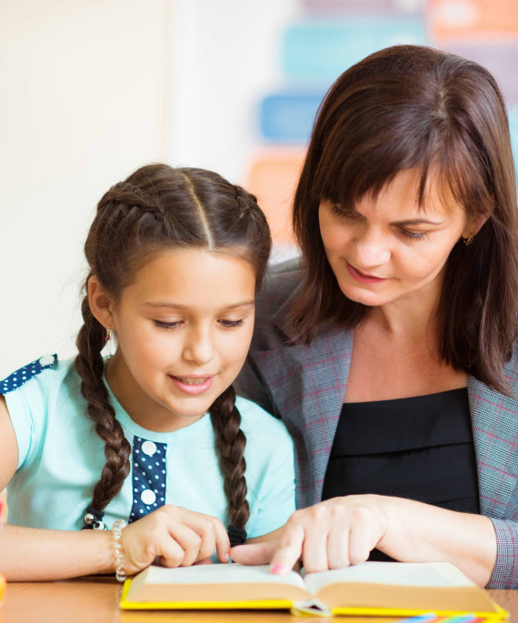 teacher tutoring a child in reading at a school desk