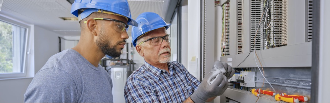 Two men in hard hats working on an electrical circuit