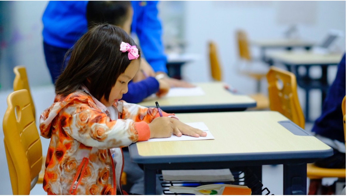 child working at school desk in orange jacket