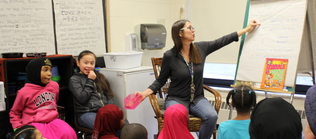 Teacher at the front of a classroom pointing to board